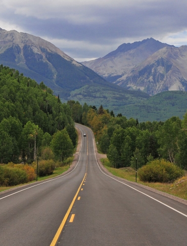 A wide shot of winding roads surrounded by trees and a view of the Colorado mountains