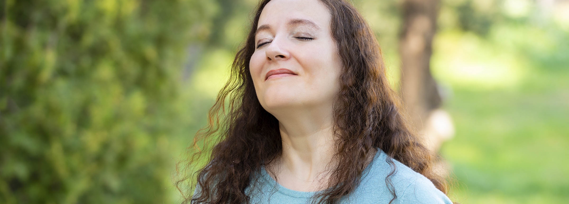 A woman with her eyes closed out in the greenery